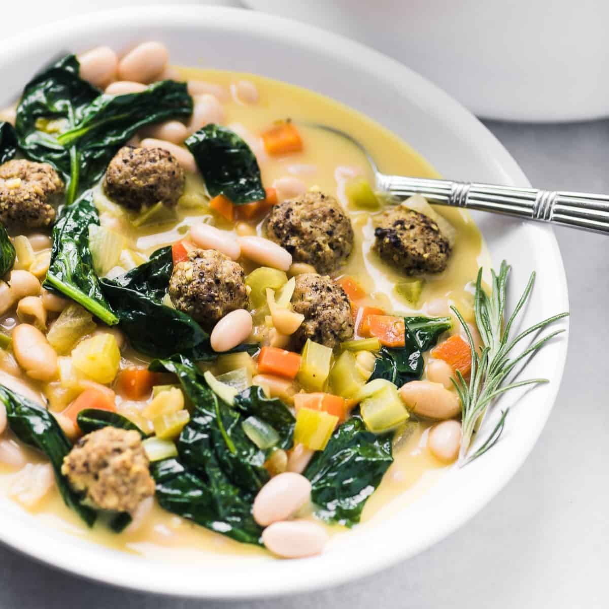 Close up of Italian White Bean Soup with Sausage Meatballs in a bowl with a spoon.