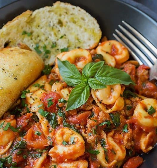 Close up of One Pan Turkey Sausage Tortellini in a dish with garlic bread and a fork.