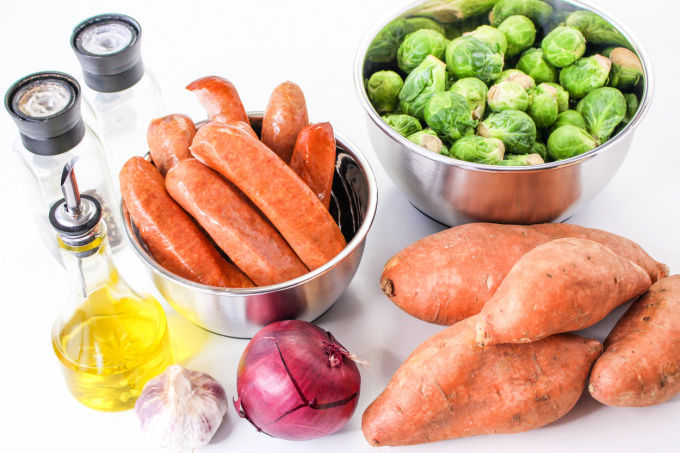 Ingredients to make Chicken Apple Sausage Dinner including sausage, sweet potatoes, garlic, onion, and brussels sprouts.