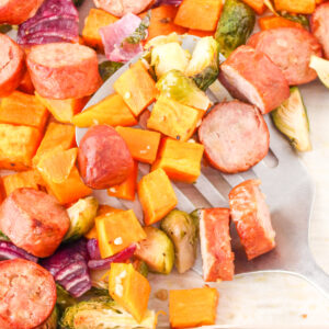 Close up of Chicken Apple Sausage and Vegetables on a baking sheet with a spatula.