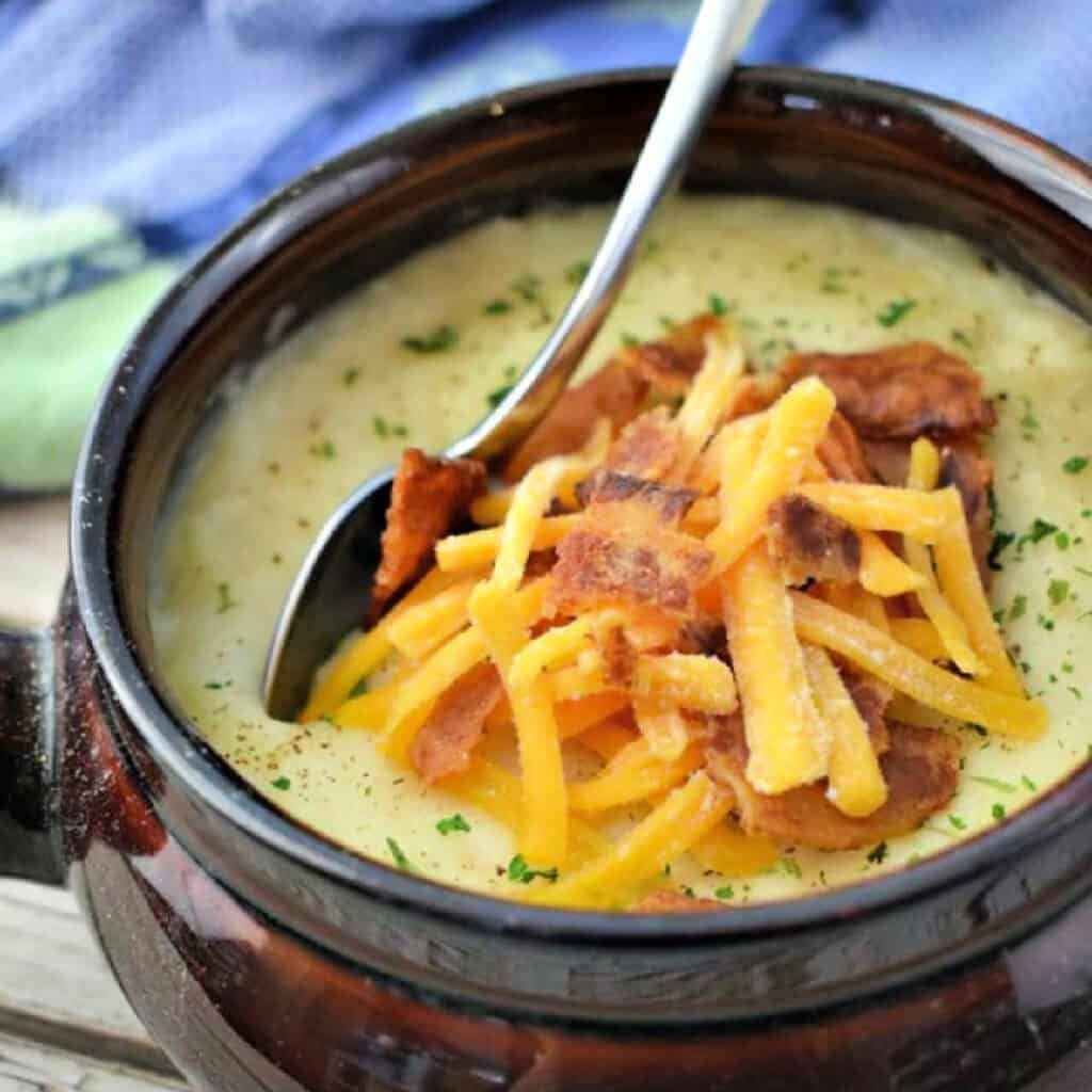 Slow Cooker Potato Soup in a brown crock topped with cheese and bacon.