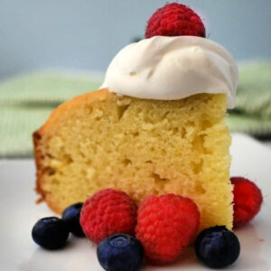 A slice of Yogurt Cake on a plate with whipped cream and berries.