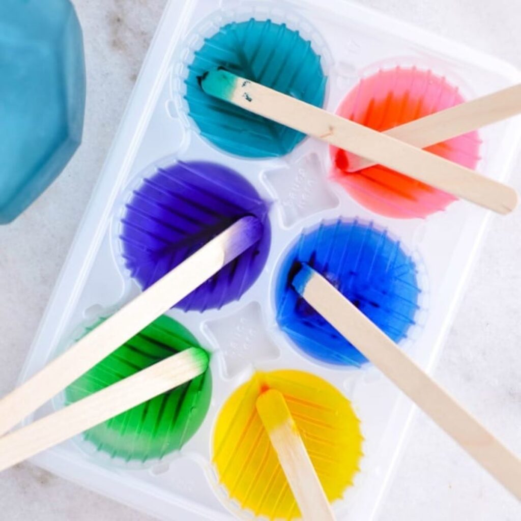 Colored liquid in an ice cube tray with wooden craft sticks.
