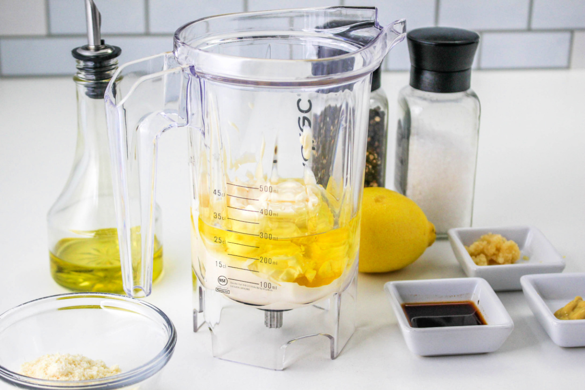 Ingredients to make creamy Caesar dressing without anchovies including olive oil, parmesan cheese, lemon, and garlic.