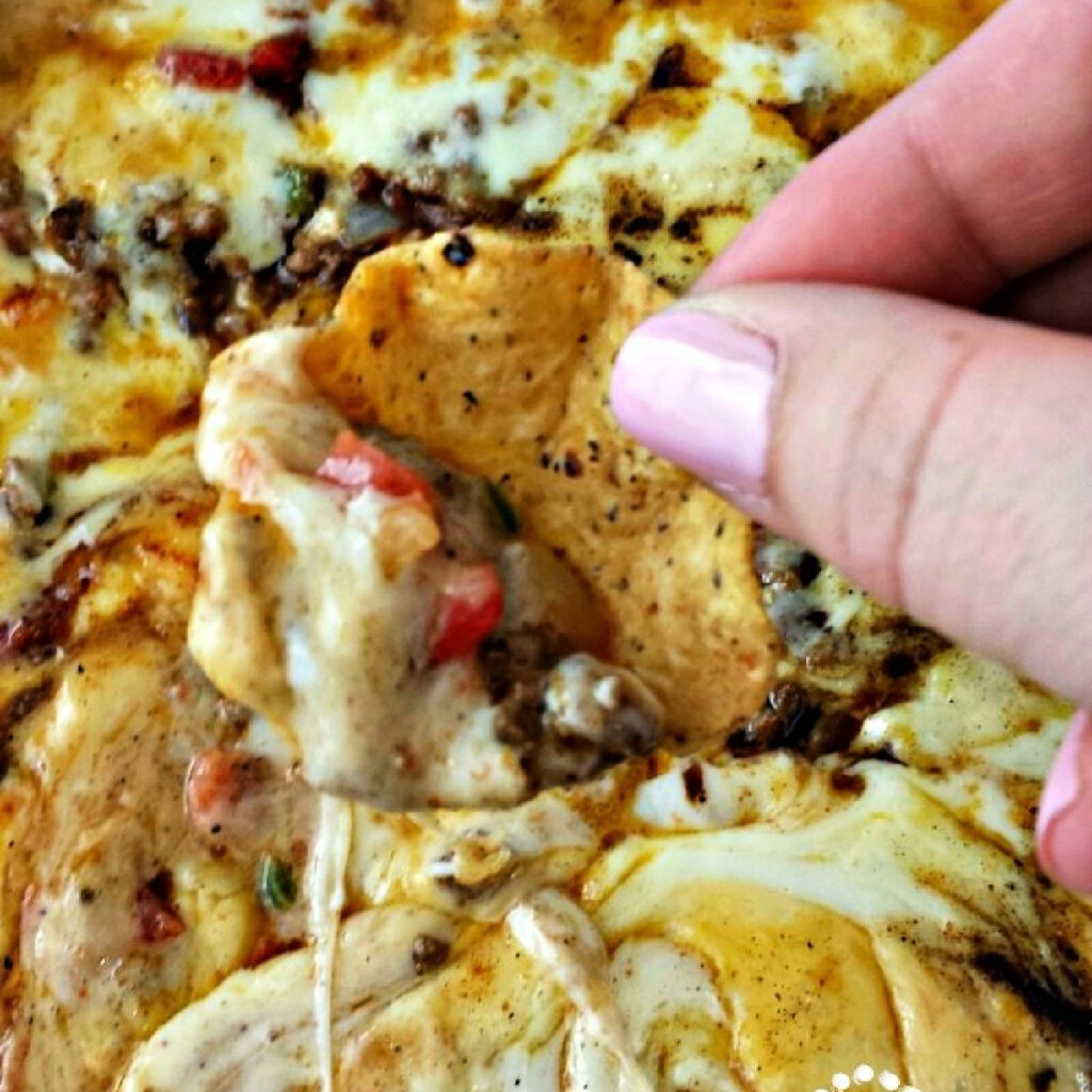 Hand scooping Nacho Skillet Dip with a tortilla chip.