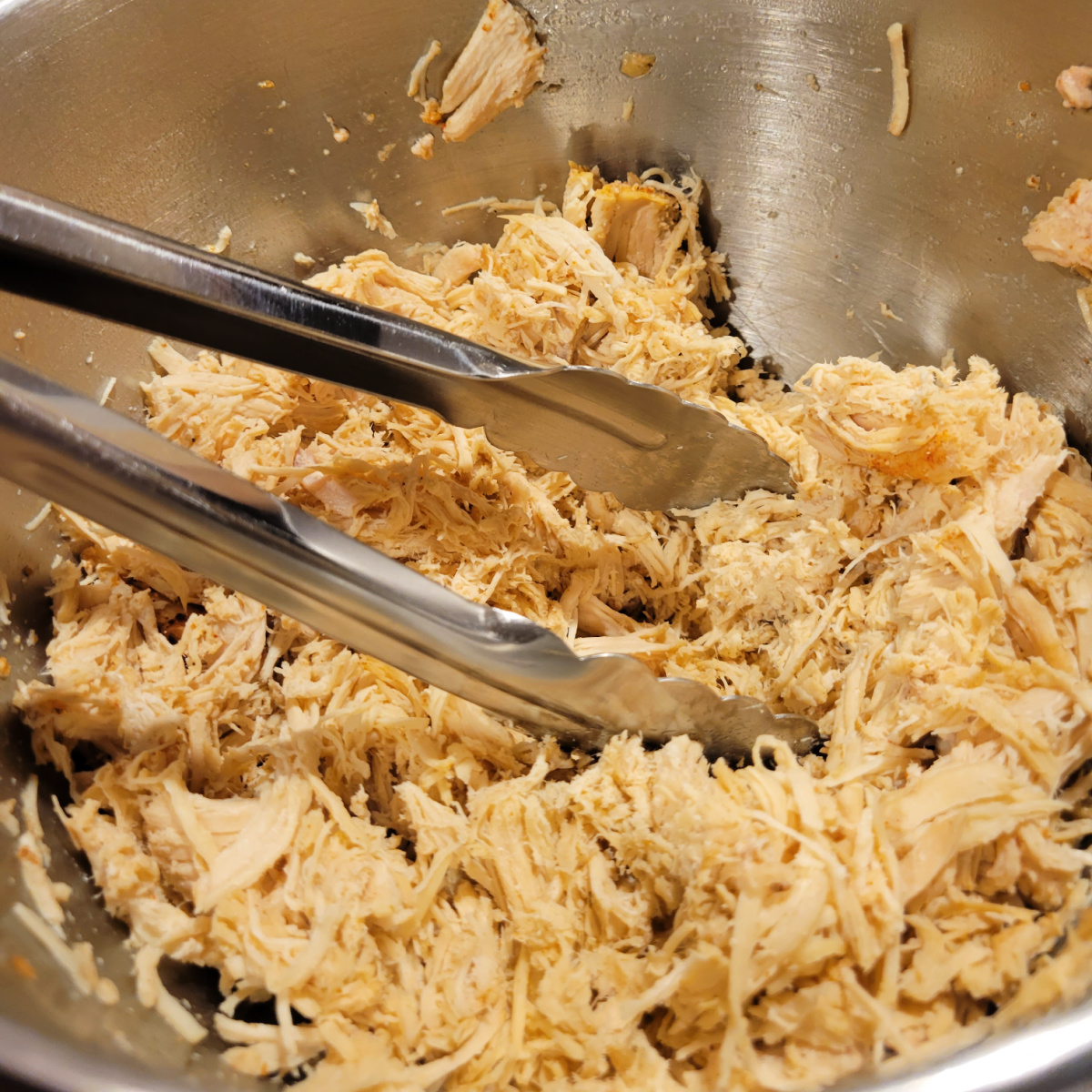 Close up of shredded chicken with tongs.