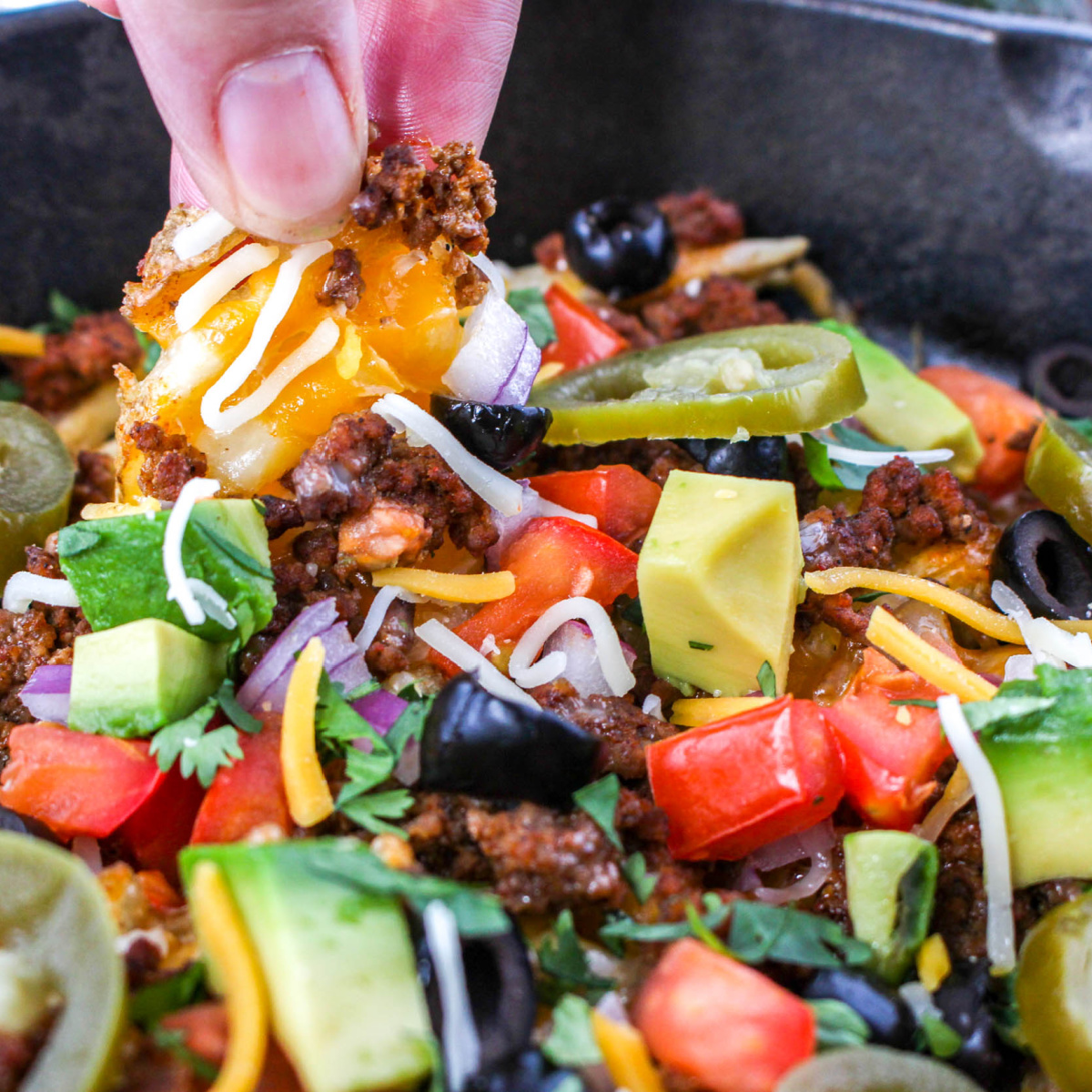 Close-up of hand scooping cheesey fry and toppings from a cast iron skillet.