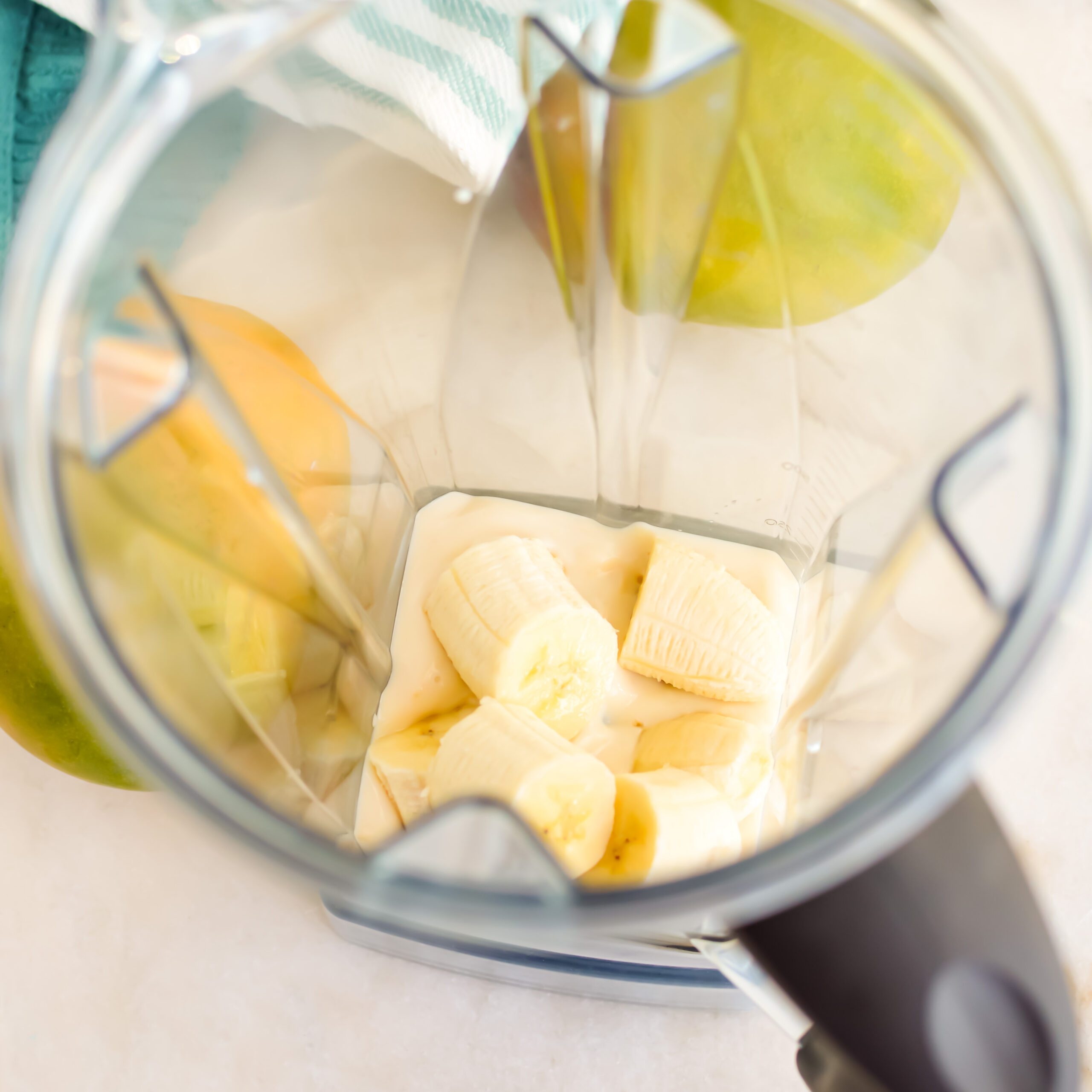 Top down view of blender with yogurt and bananas for making a strawberry mango smoothie.