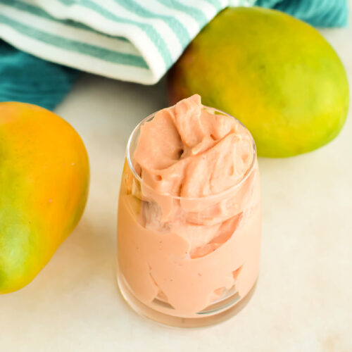 Creamy Strawberry Mango Smoothie in a small glass next to fresh mangoes.