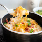 Spoon with a bite of Crockpot Hashbrown Soup over a bowl.