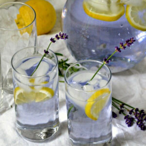 Tall glasses of Lavender Lemonade garnished with lemon and a stem of lavender.