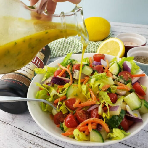 Cruet with Lemon Vinaigrette Salad Dressing drizzling onto salad.