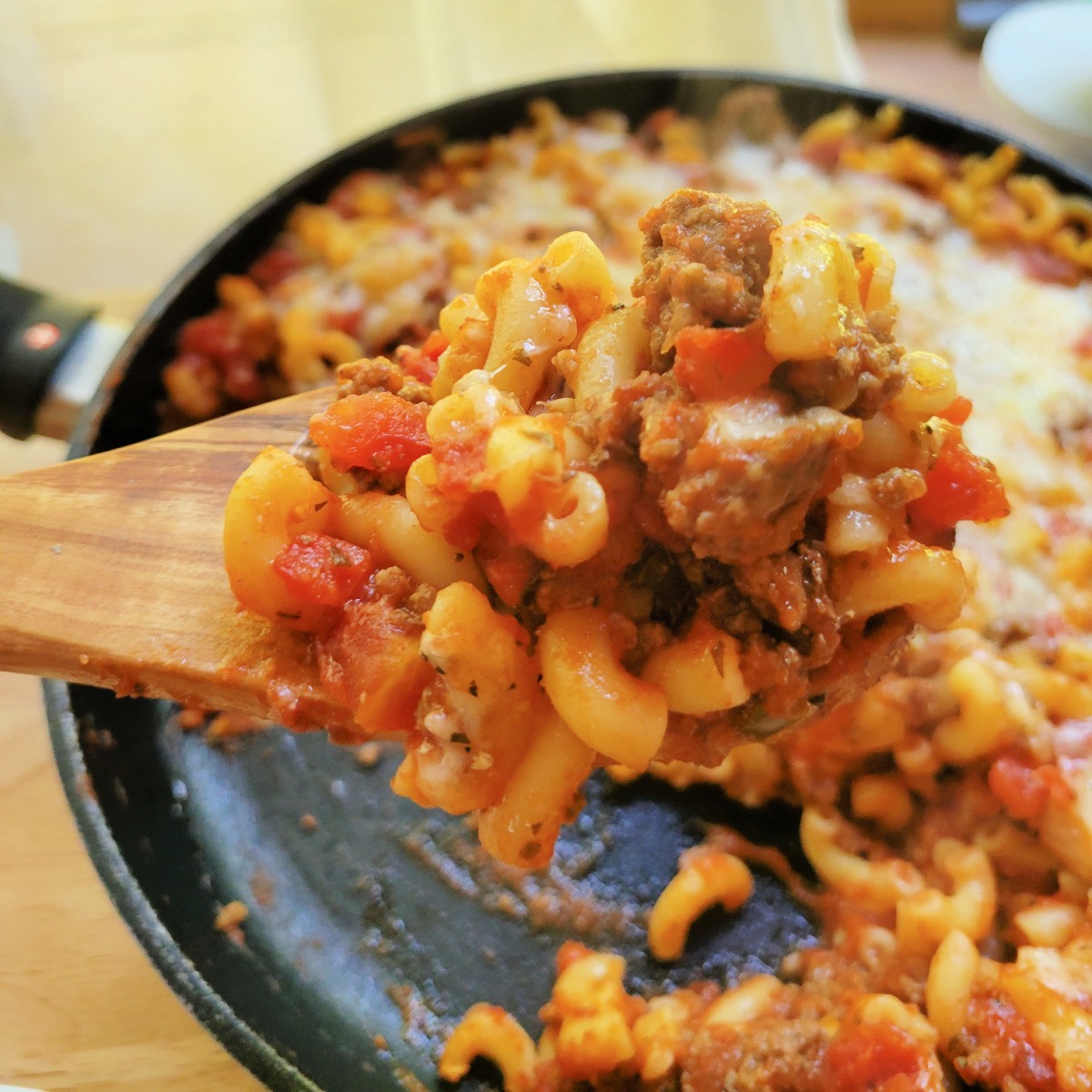 Wooden spoon scooping American Chop Suey from a skillet.