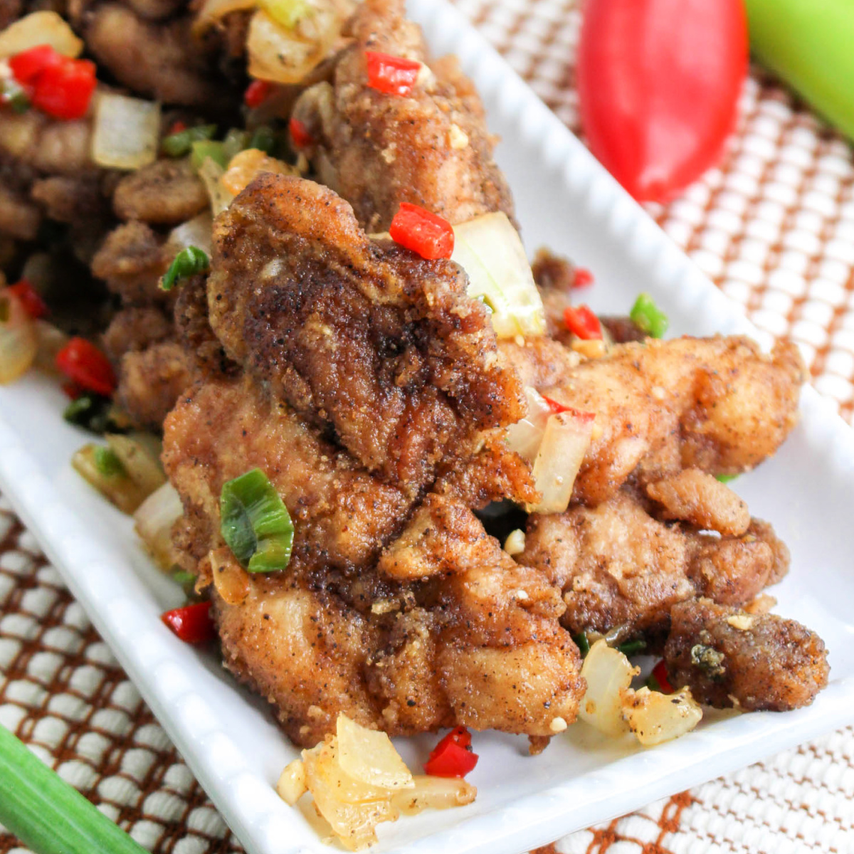 Crispy Salt and Pepper Chicken with spring onions on a white platter.