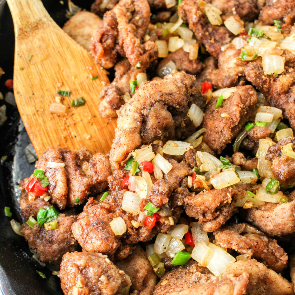 Salt and Pepper Chicken Stirfry in a skillet with a wooden spoon.