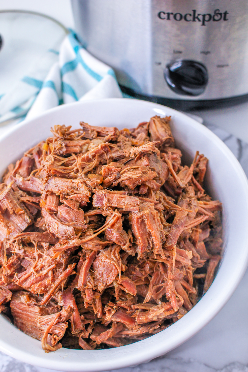 Close up of Slow Cooker Shredded Beef with a Crockpot in the background.