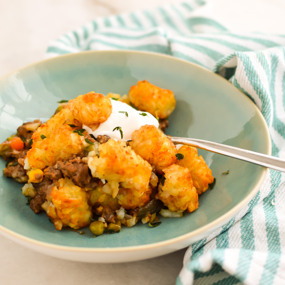 Tater Tot Sheperds Pie topped with sour cream in a bowl with a spoon.