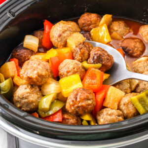 Sweet and Sour Meatballs in a crock pot with pineapple, peppers, and onions.