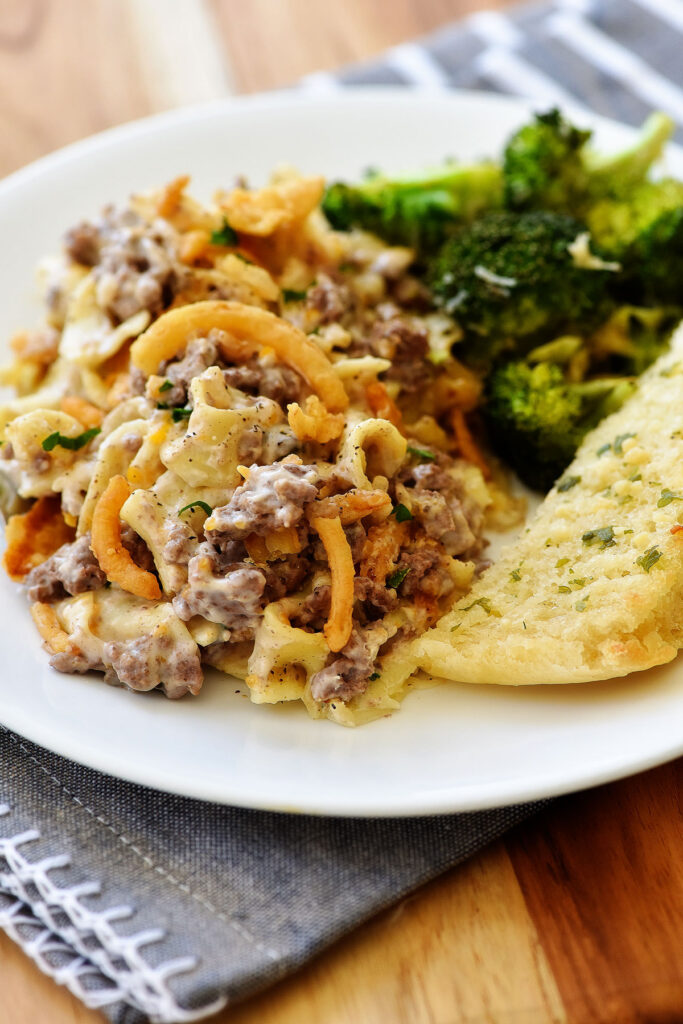 French Onion Noodle Casserole on a plate with garlic bread and broccoli.