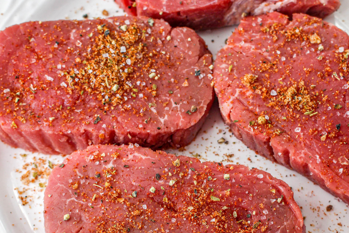 Seasoned raw sirloin steaks on a white plate.