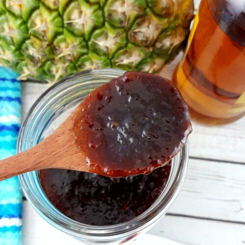 Pineapple Bourbon BBQ Sauce on a wooden spoon over a jar.