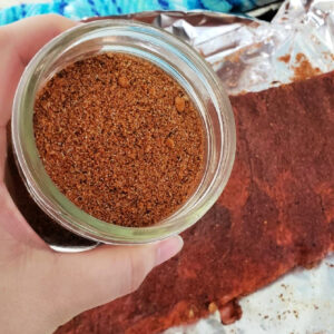 Pork Rub Seasoning in a jar held by a hand over ribs.