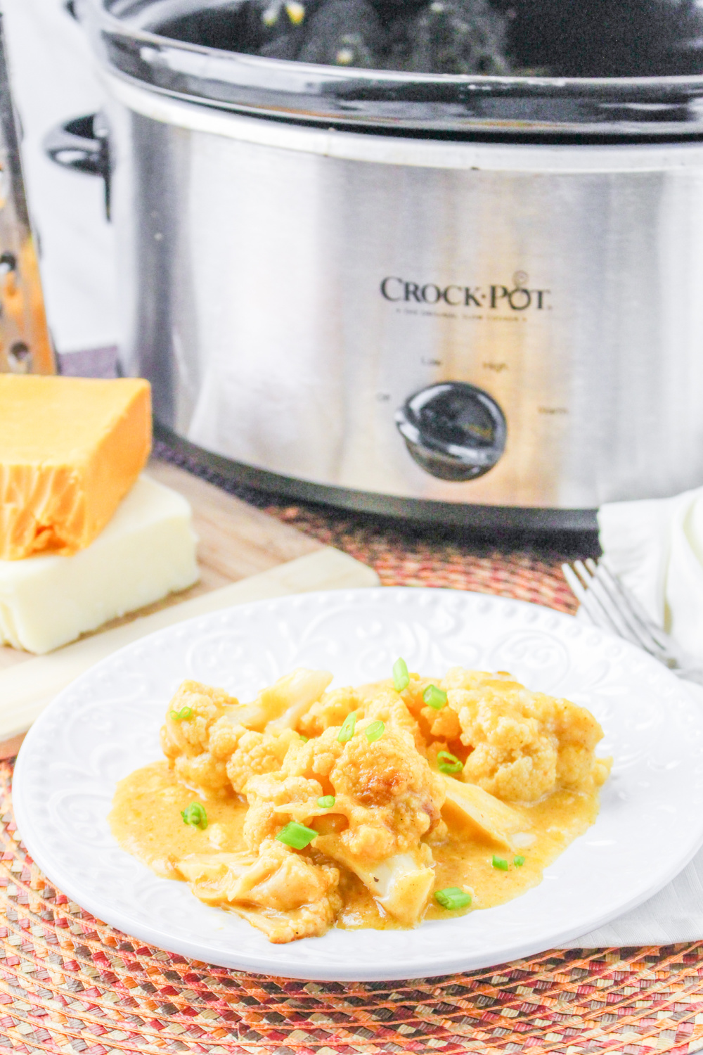 Crockpot Cauliflower on a white plate with a slow cooker in the background.