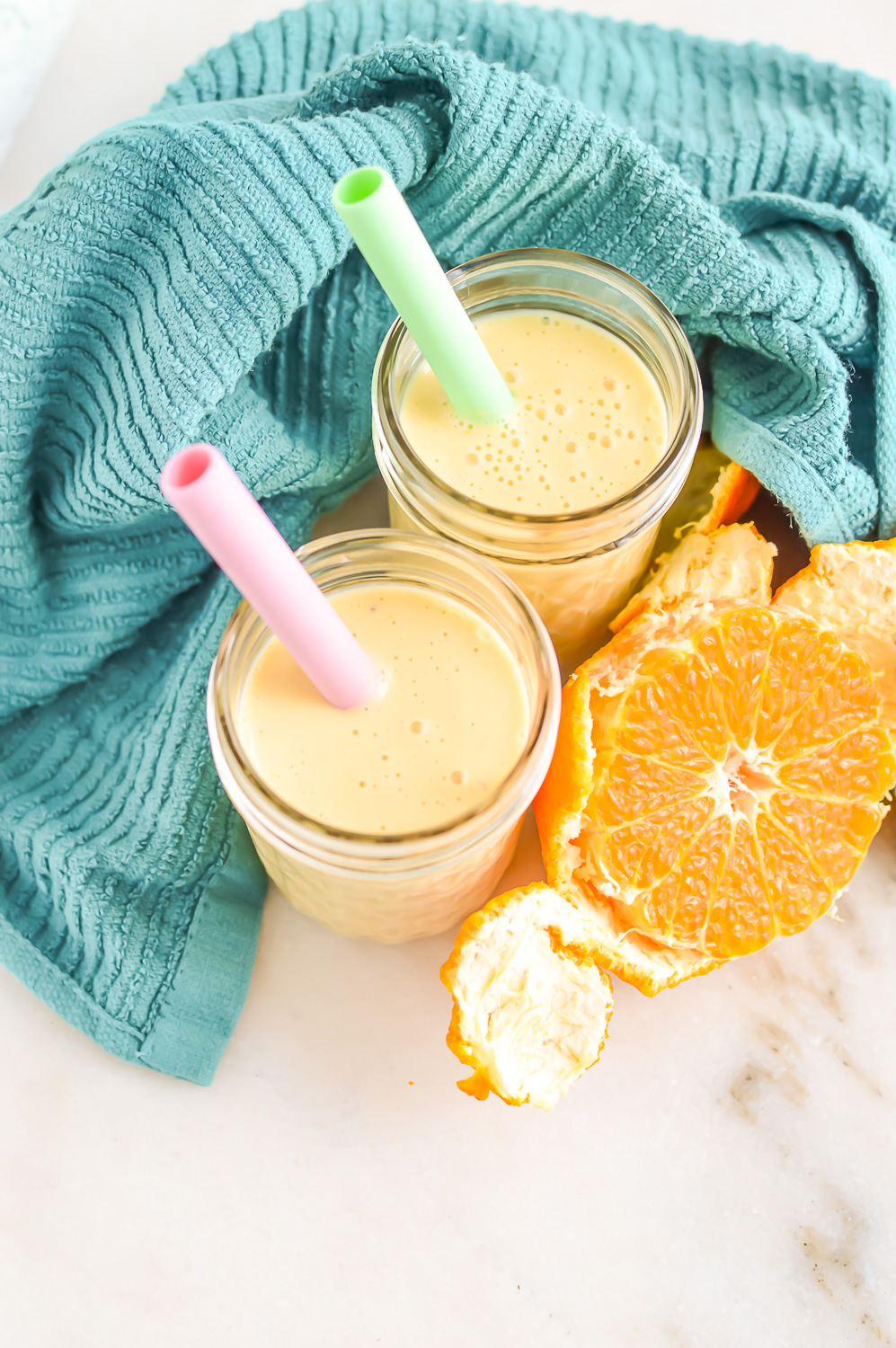 Two Banana Orange Smoothies with straws next to an orange.