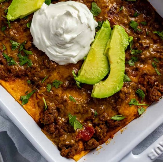 Layered Enchilada Casserole with avocado and sour cream on top.