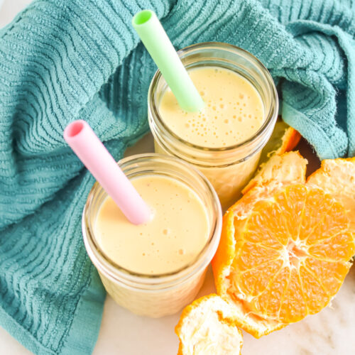 Two Orange Banana Smoothies with straws next to an orange.