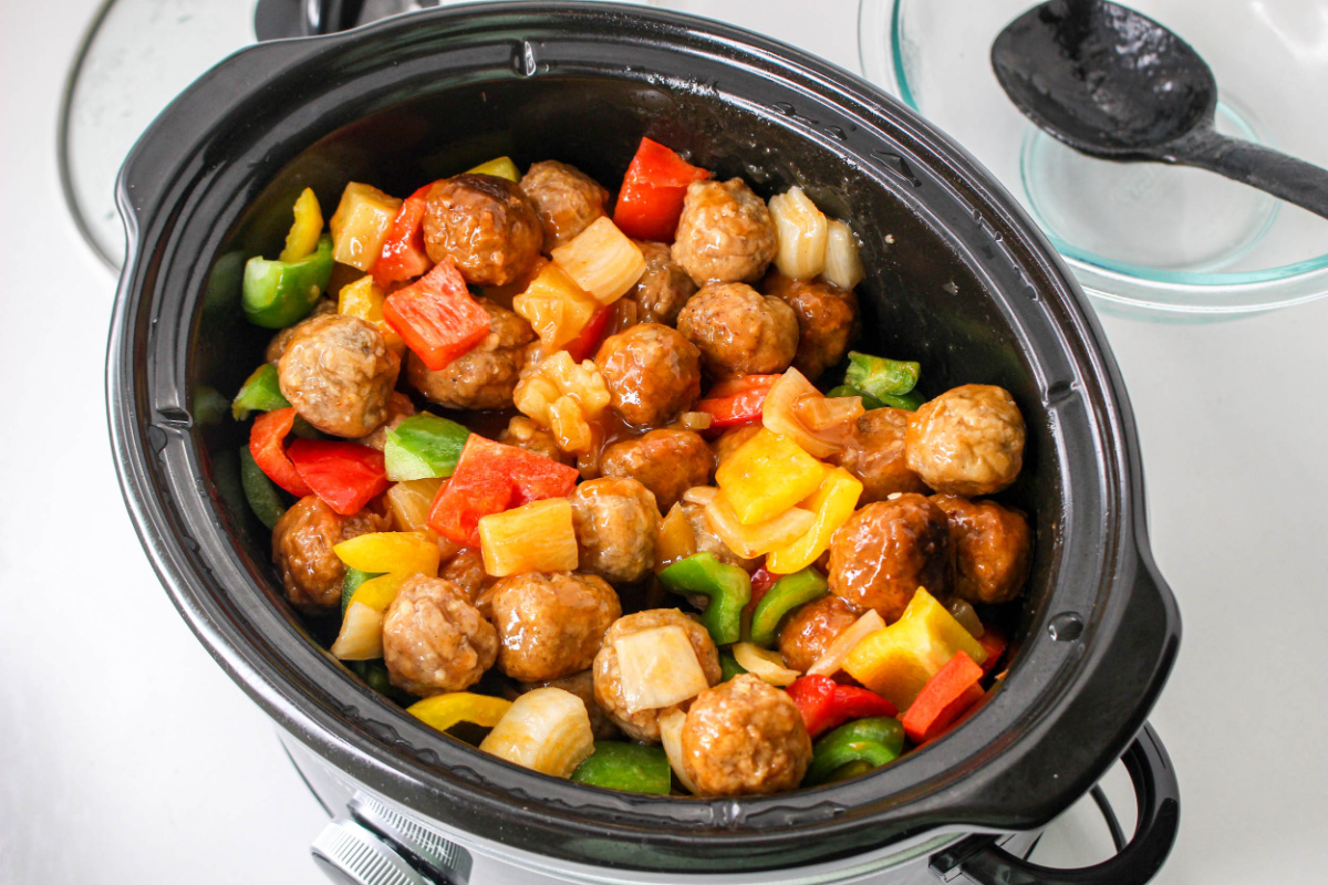 Sweet and Sour Meatballs in a black crockpot with peppers, pineapple and onions.