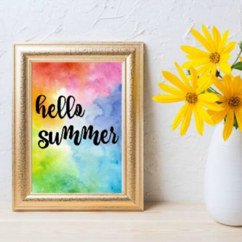 Hello Summer Printable in a gold frame next to a vase of yellow flowers.