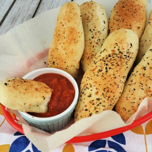 Italian breadsticks in a basket with marinara sauce.
