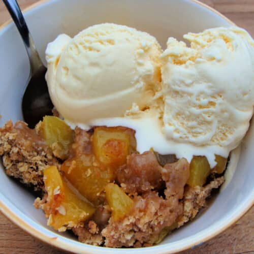 Peach Crisp in a bowl with vanilla ice cream.