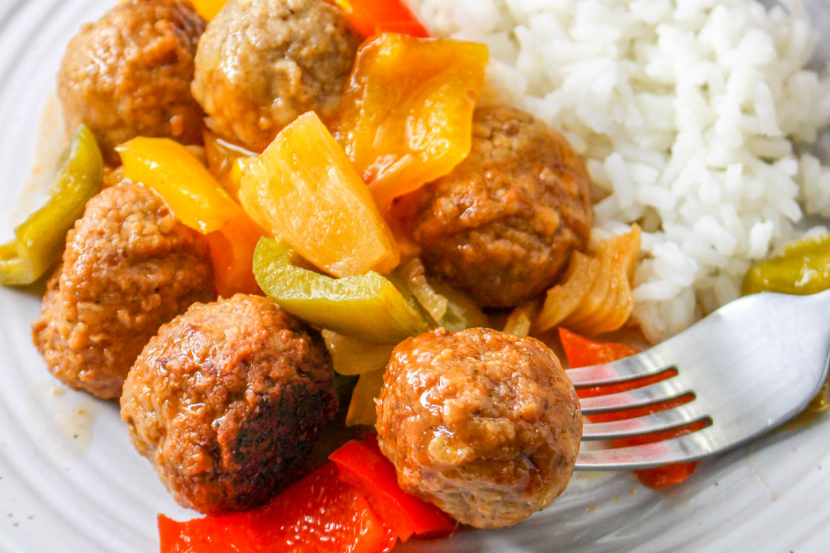 Slow Cooker Sweet and Sour Meatballs on a plate with a fork and white rice.