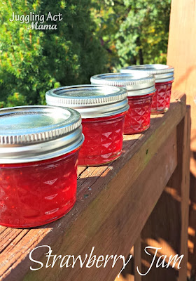 small jars of strawberry jam sitting on a wooden railng
