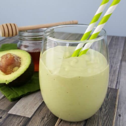 Avocado Smoothie in a glass with two striped straws.