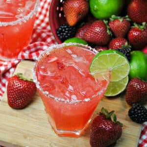 Berry Margarita garnished with lime next to fresh berries on a cutting board.