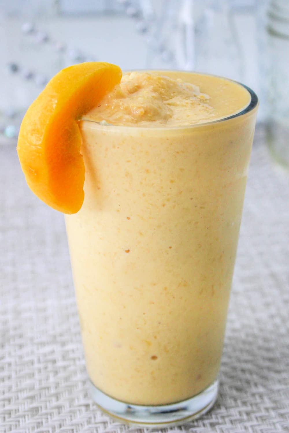 Tall glass of Orange Peach Smoothie garnished with a slice of fresh peach.