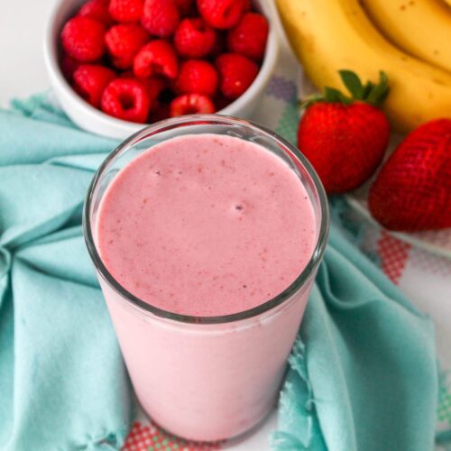 Raspberry Banana Smoothie in a tall galss next to fresh fruit.