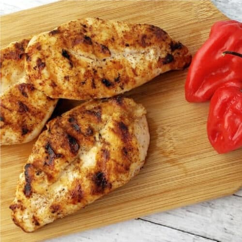 Spicy Grilled Chicken on a cutting board next to hot peppers.