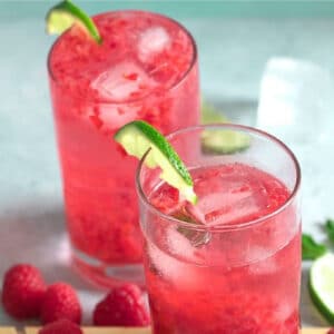 Raspberry Mojitos in tall glasses garnished with limes.