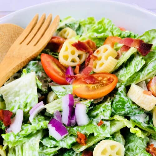 BLT Pasta Salad Recipe in a bowl with wooden serving utensils.