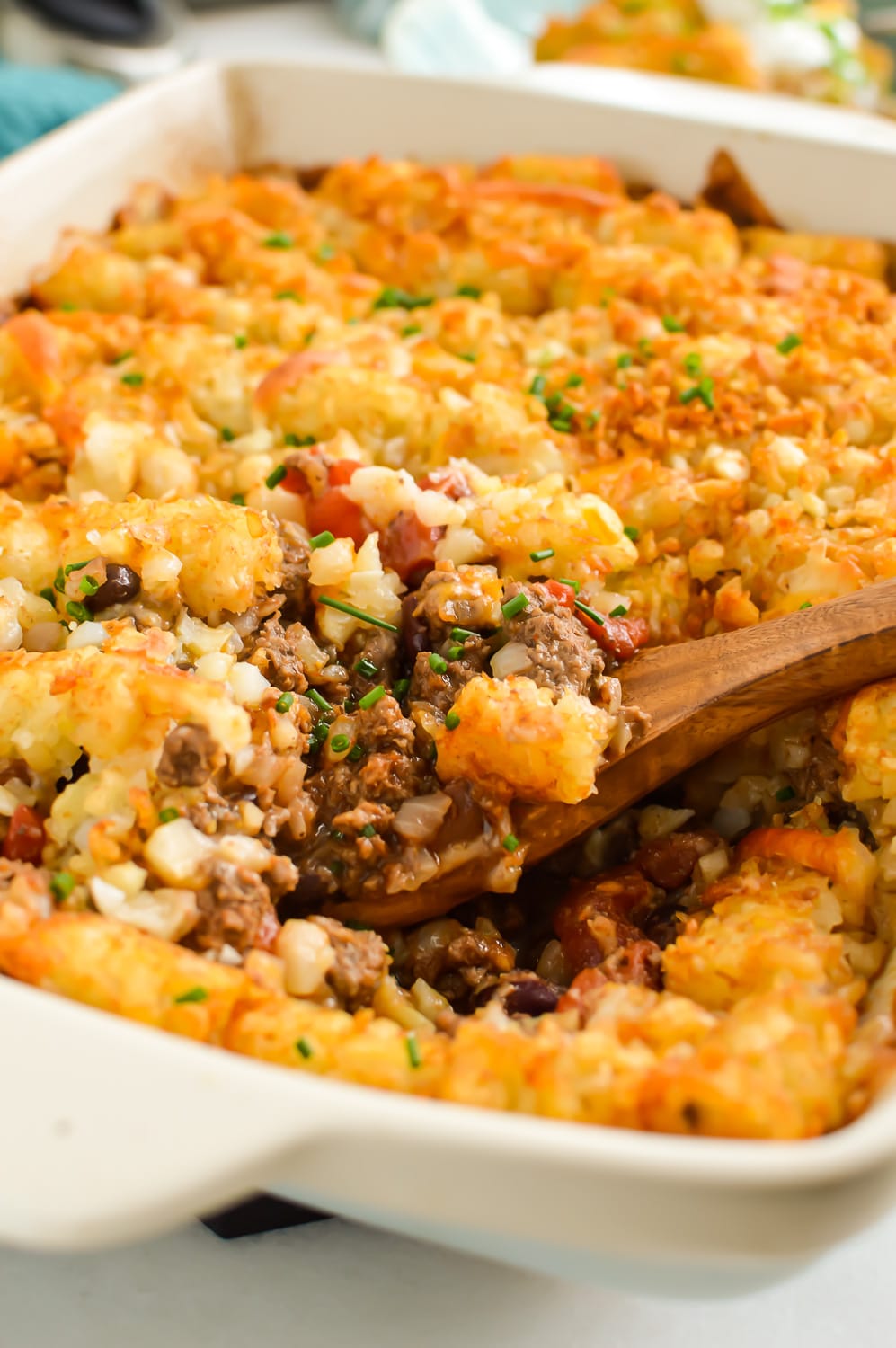 Beef chili tater tot casserole with a wooden spoon.
