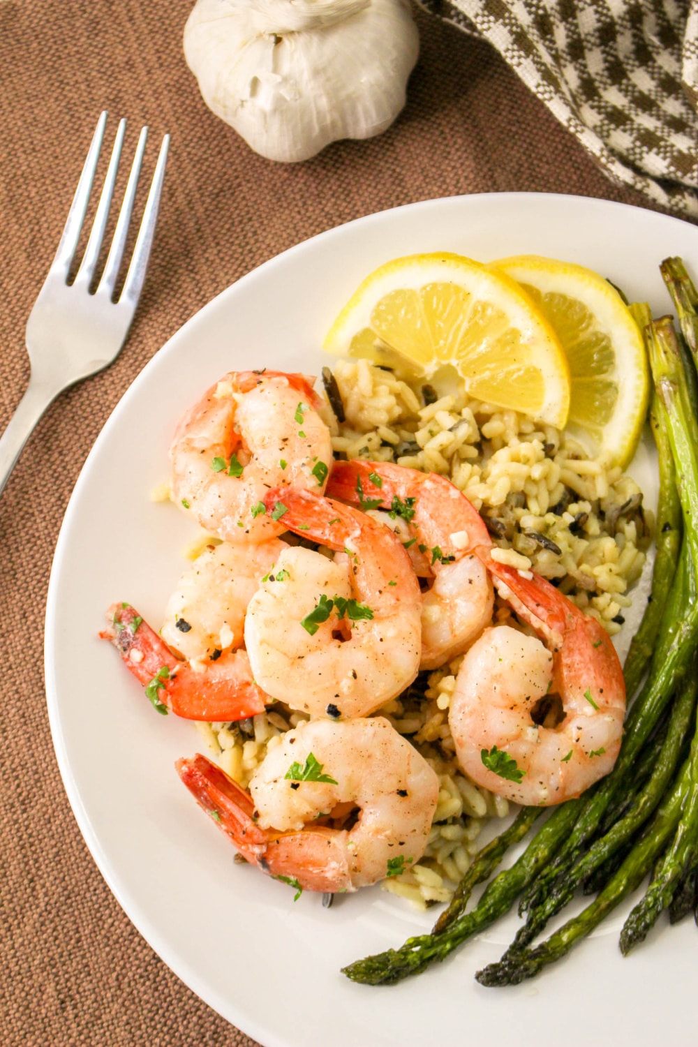 Lemon Garlic Butter Shrimp on a plate with lemon, rice, and asparagus.