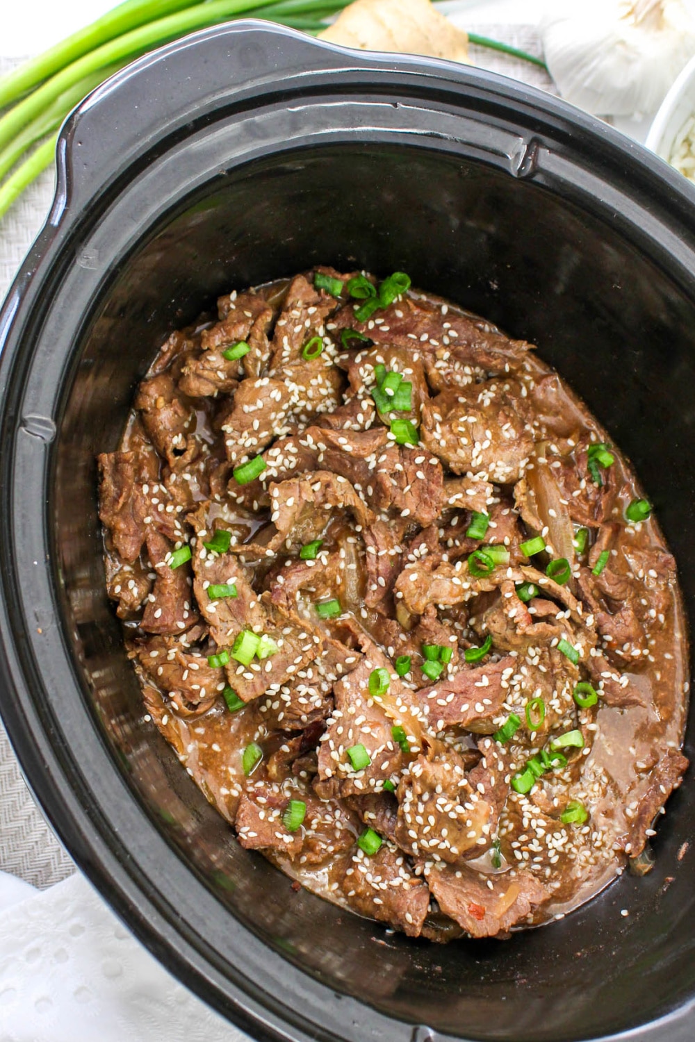 Slow Cooker Korean Beef with green onions and sesame seeds in a crockpot.