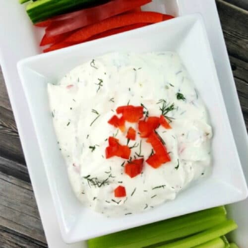 Greek veggie dip garnished with dill and diced peppers.