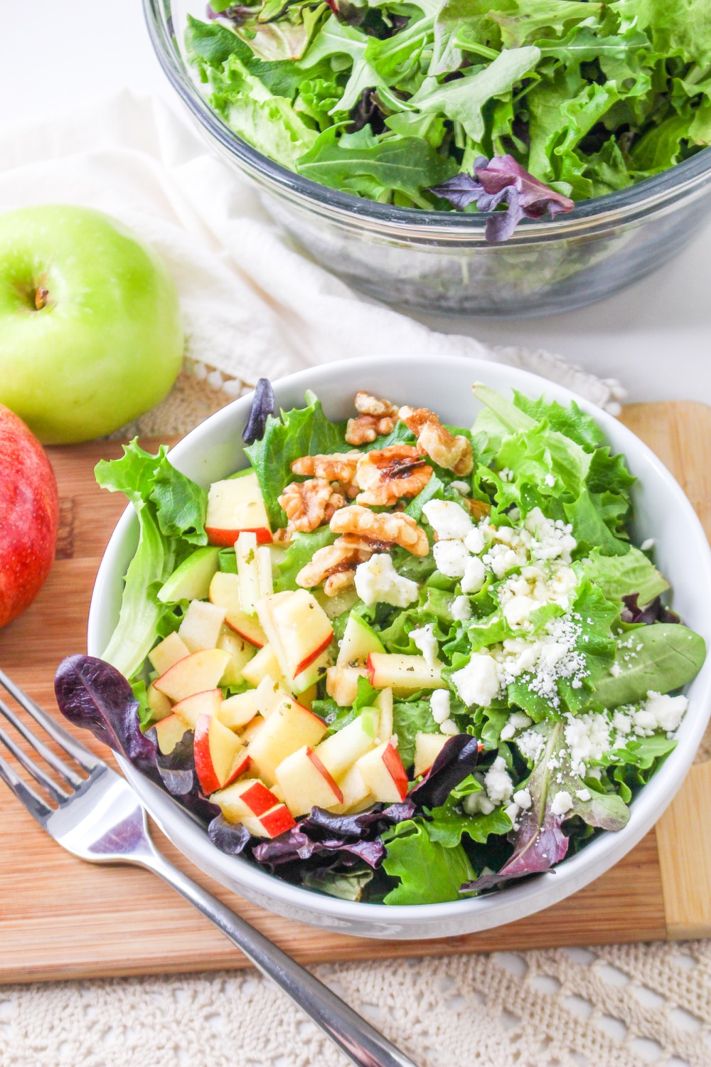 Bowl of Apple Feta Salad on a cutting board next to apples and a bowl of greens.