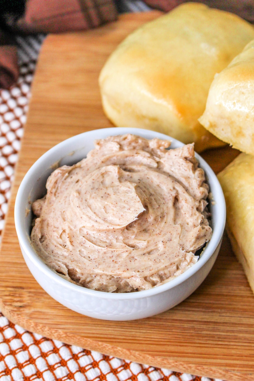 Copycat Texas Roadhouse Butter in a bowl on a cutting board with rolls.