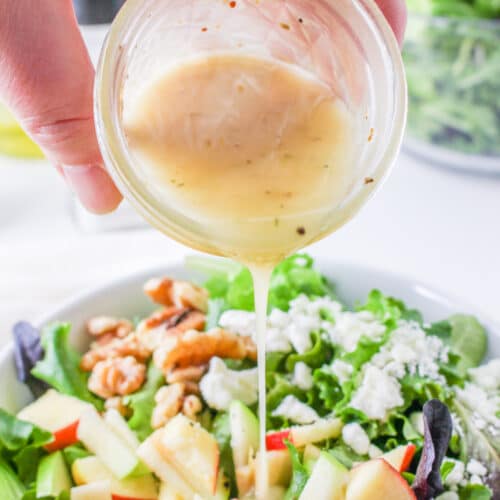 Hand pouring lemon mustard vinaigrette from a mason jar onto a salad.